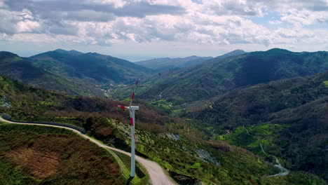 toma aérea hacia atrás de un idílico paisaje montañoso y una turbina eólica giratoria que produce energía en la naturaleza - día nublado y luz solar