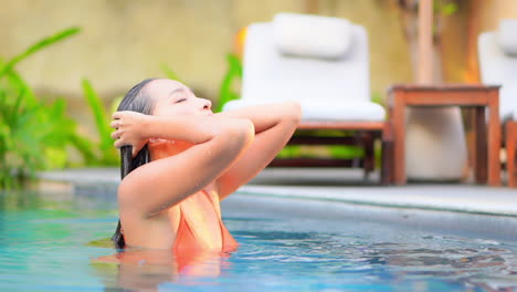 Nahaufnahme-Einer-Hübschen-Frau,-Die-Aus-Dem-Wasser-Eines-Resort-Swimmingpools-Auftaucht-Und-Ihr-Nasses-Haar-Aus-Dem-Gesicht-Streicht