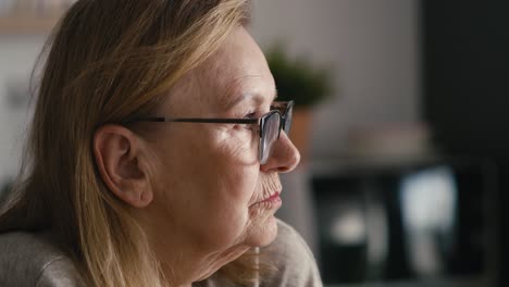 Extreme-close-up-of-thoughtful-caucasian-senior-woman-sitting-in-armchair-and-looking-aw