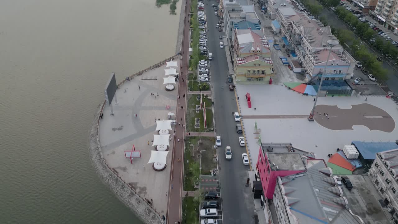 Aerial footage of a broad walk and a road along shops located at Mingle Lake in Daqing, Heilongjiang District in China.