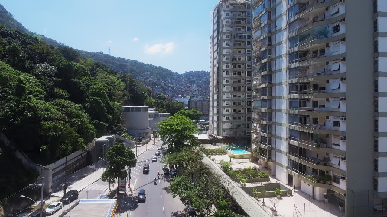 Vista aérea avançando ao longo de edifícios residenciais com piscinas e montanhas no Rio.