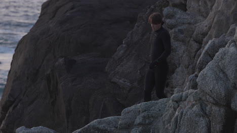 Adult-male-climbs-cliff-and-cliff-jumps-off-into-the-ocean-at-sunset