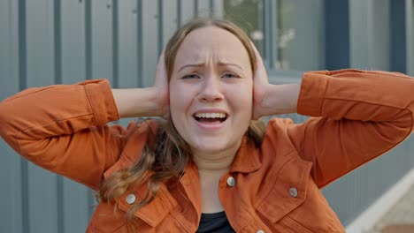 mujer caucásica cubriendo sus orejas con las manos, gritando de angustia