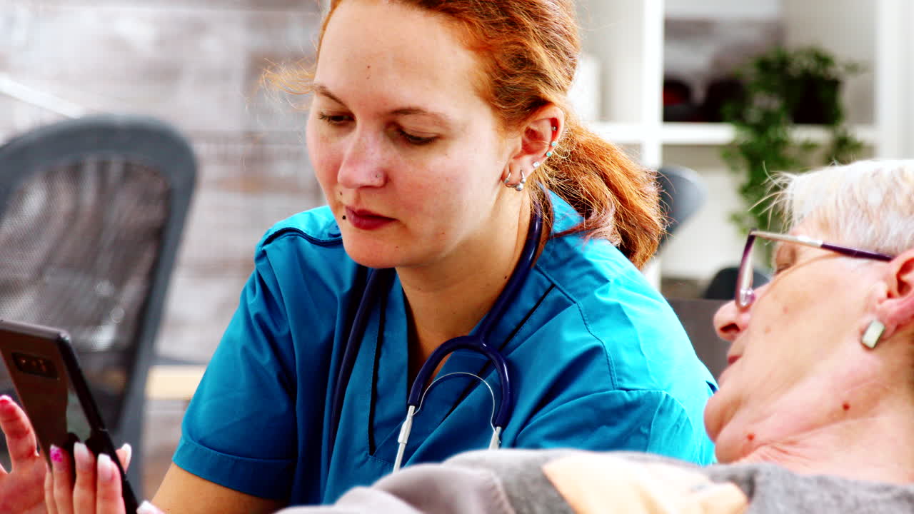 Nahaufnahme einer Krankenschwester, die einer älteren, behinderten Frau hilft, ein Smartphone zu bedienen.