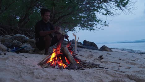 a cinematic professional shot of a spear fisherman with a fish walking up the beach to his fire and sitting down to prepare to cook his fish