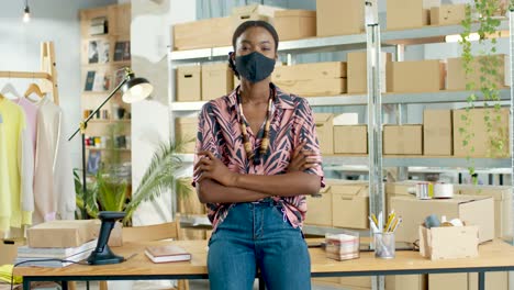 african american woman designer in black mask looking at camera in positive mood in clothing store