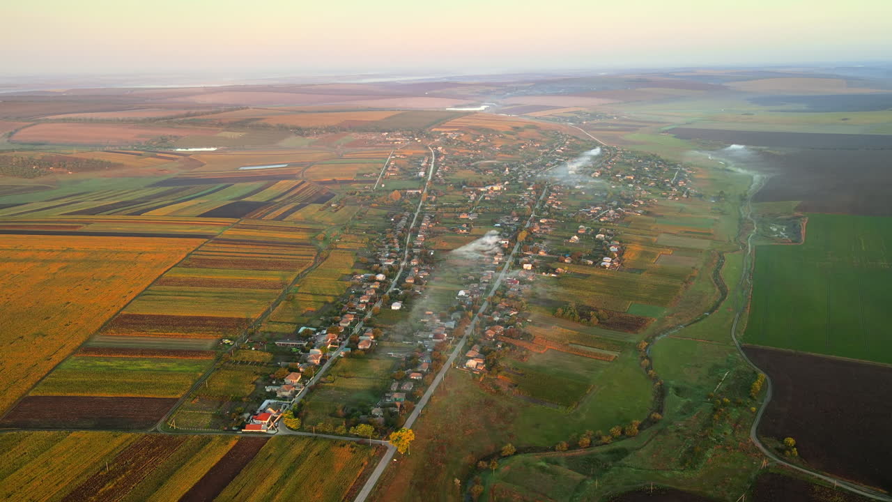 Aerial drone view of village in Moldova at sunset. Few columns of smoke from fires, wide fields