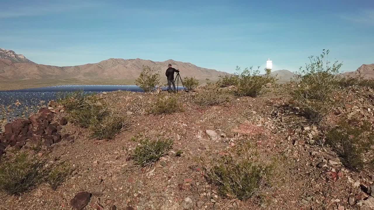 Veduta aerea con drone di un fotografo in piedi sulla cima di una collina che si affaccia su un enorme impianto solare a Primm, Nevada.