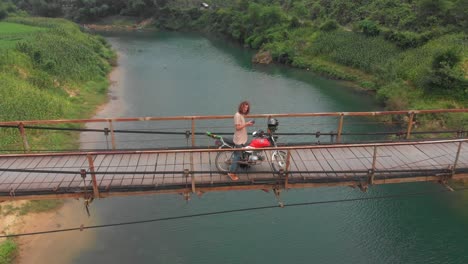 man is standing with motorbike on old suspension bridge at vietnam, aerial