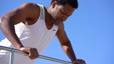 hombre deportivo sonriente entrenando en la barandilla contra el cielo azul