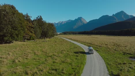 vuelo aéreo siguiendo una caravana turística en una remota carretera rural en los alpes del sur paisaje montañoso de glenorchy, isla sur de nueva zelanda aotearoa