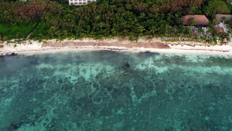 Trucking-right-aerial-bird's-eye-drone-view-of-a-beautiful-tropical-vacation-beach-with-crystal-clear-blue-water,-white-sand,-palm-trees,-lounge-chairs-at-a-resort-in-Riviera-Maya,-Mexico-near-Cancun