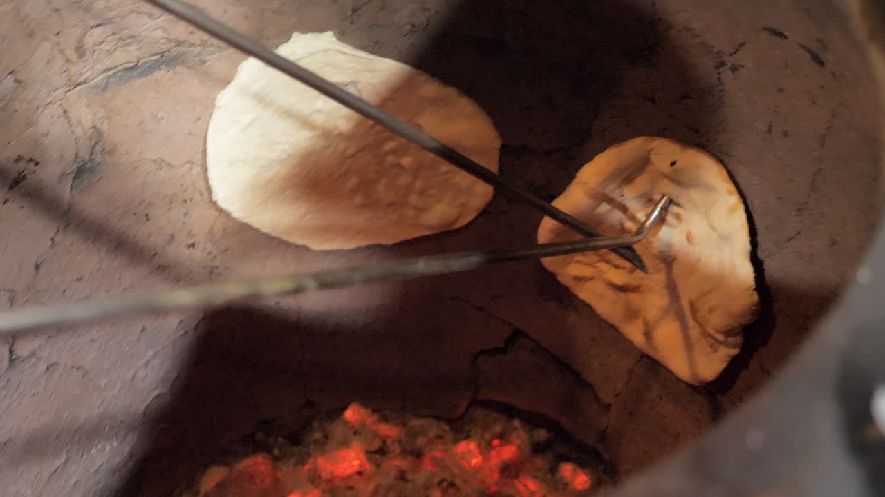 el chef quita el naan cocido del horno tandoor tradicional, el pan plano indio hornea y las burbujas en el horno de olla de barro, se desliza en cámara lenta de cerca -- 4k