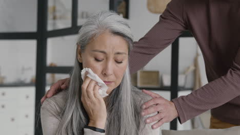 一个悲伤的中年女人哭泣,用纸巾擦拭眼泪,而她的丈夫试图安慰她