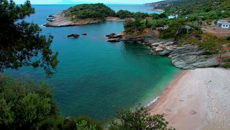 rivelazione aerea cinematografica di una spiaggia isolata con acque turchesi, case sulla scogliera e vegetazione lussureggiante, auto grigia, spiaggia di aliki, isola di thassos, grecia