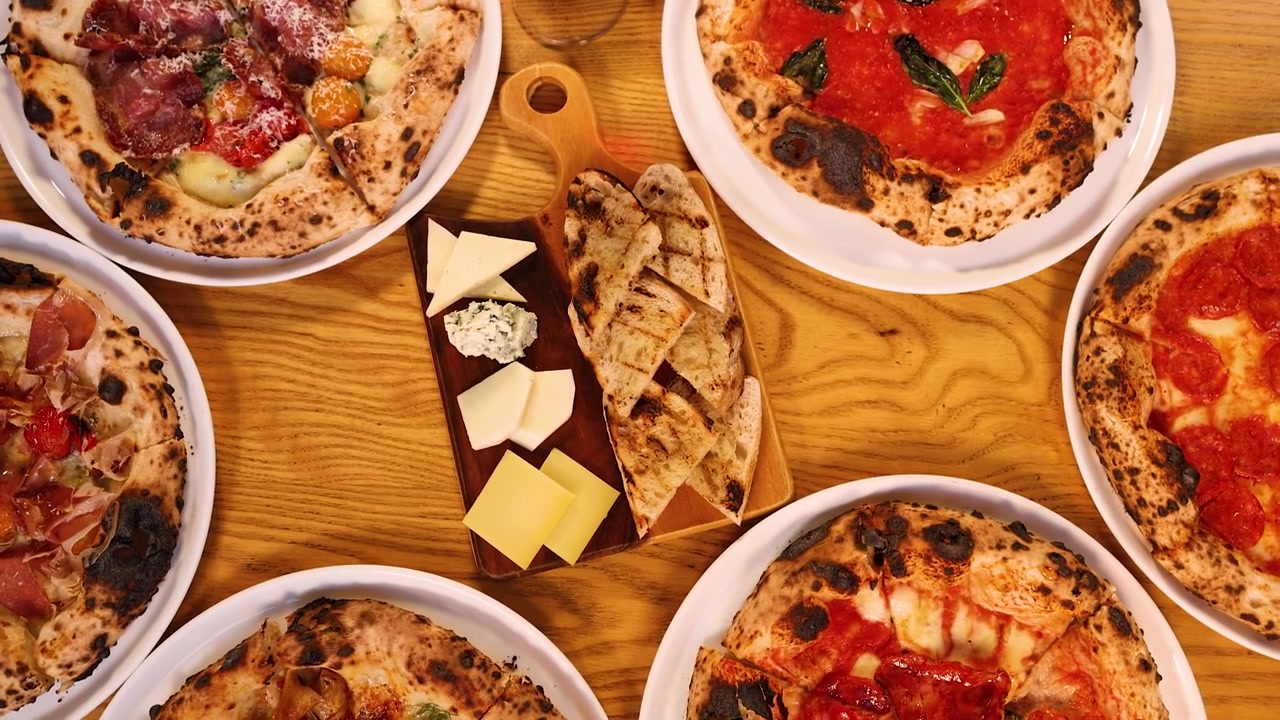 Rotazione della telecamera dall'alto su varie pizze, tagliere di formaggi e vino rosso su un tavolo di legno di ristorante