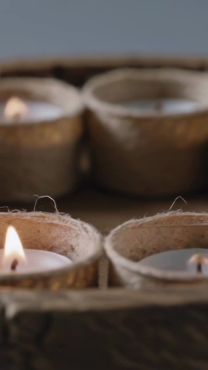 Video verticale: Accensione degli stoppini delle tealight nei vasi per piantine tramite una scintilla fuori campo su un vassoio.