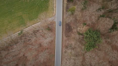 Overhead-drone-shot-tracking-a-remote-countryroad-with-one-car-passing-along