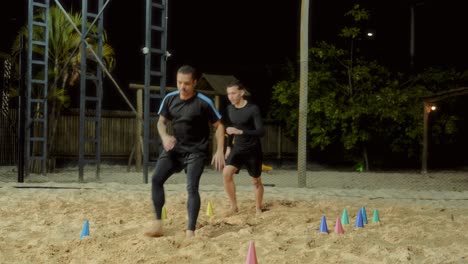 two men training and performing agility drills on sand at night