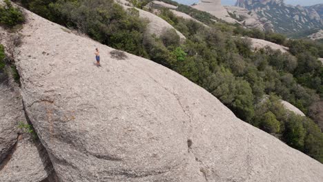 Woman-doing-yoga-at-mountain-top-of-Monastery-of-Montserrat,-Drone-shot