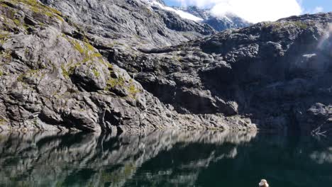 Person-resting-on-lake-shore-and-enjoying-spectacular-mountain-view-during-sunny-day-and-blue-sky---Getrude-Saddle-Track-in-New-Zealand--Rear-view