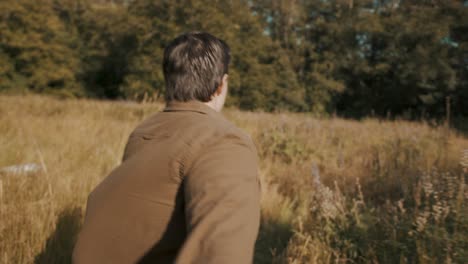pov: a young man is running and holding someone's hand, leading them through a tall grass field