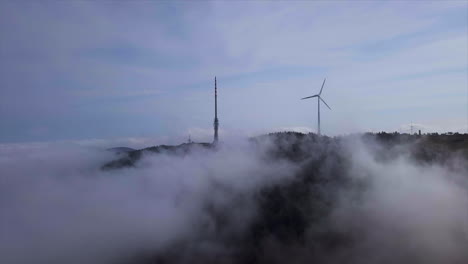 aerial shot of big broadcasting tower and wind generator wrapped in clouds over the black forest mountain hornisgrinde on a brighty day in autumn