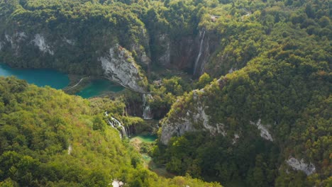 incredible aerial drone view of bright turquoise lakes connected with waterfalls between rocky cliffs and dense forest