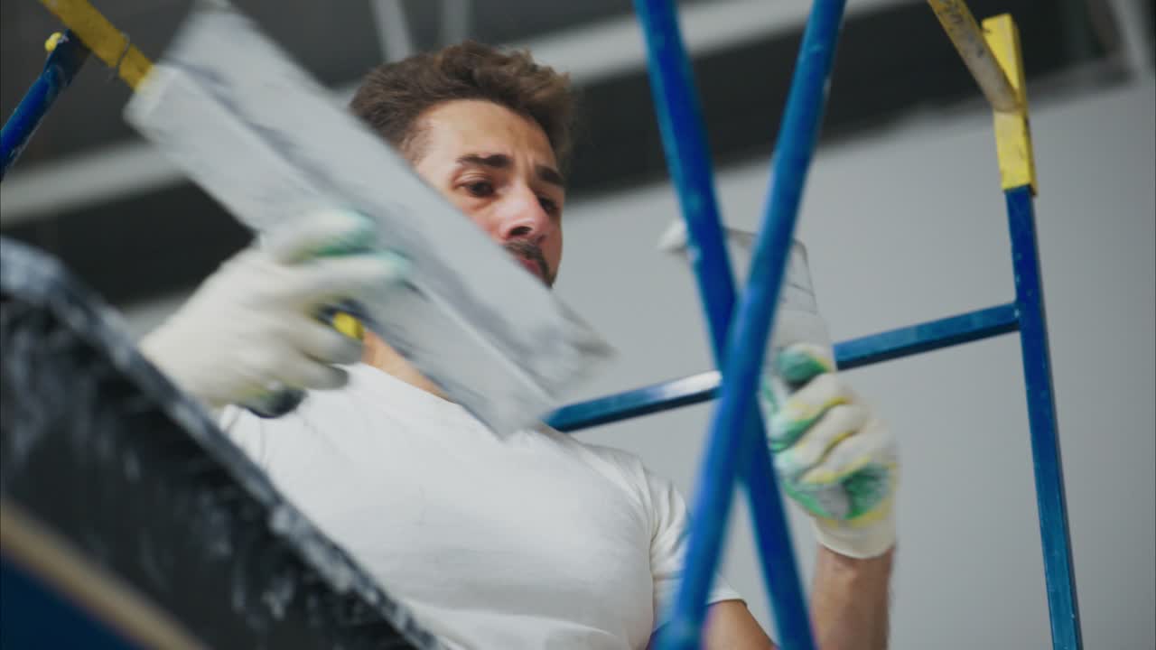 A Dedicated Worker Engaged in Painting a Wall while Balancing on a Ladder, Showcasing Precision in Home Renovation and Craftsmanship Skills