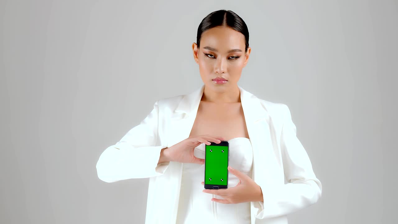 아름다운 아시아 사업가 여성이 녹색 화면의 스마트폰을 보여주고 카메라를 보고 있습니다.