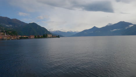 Una-Toma-Panorámica-Del-Lago-De-Como,-Italia,-Con-Un-Colorido-Pueblo-Y-Montañas-Al-Fondo