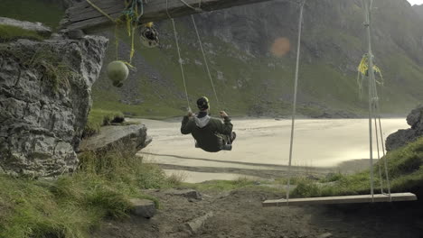 A-man-swinging-at-Kvalvika-beach-and-enjoying-the-view-in-Lofoten,-Norway