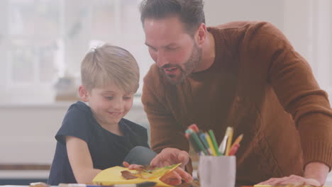 padre con hijo en casa haciendo artesanía y haciendo imágenes de hojas en la cocina