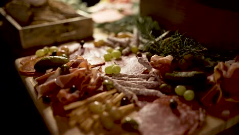 cold cuts, grapes breadsticks and prosciutto appetizer on cutting board with rosemary herbs, close up dolly out shot