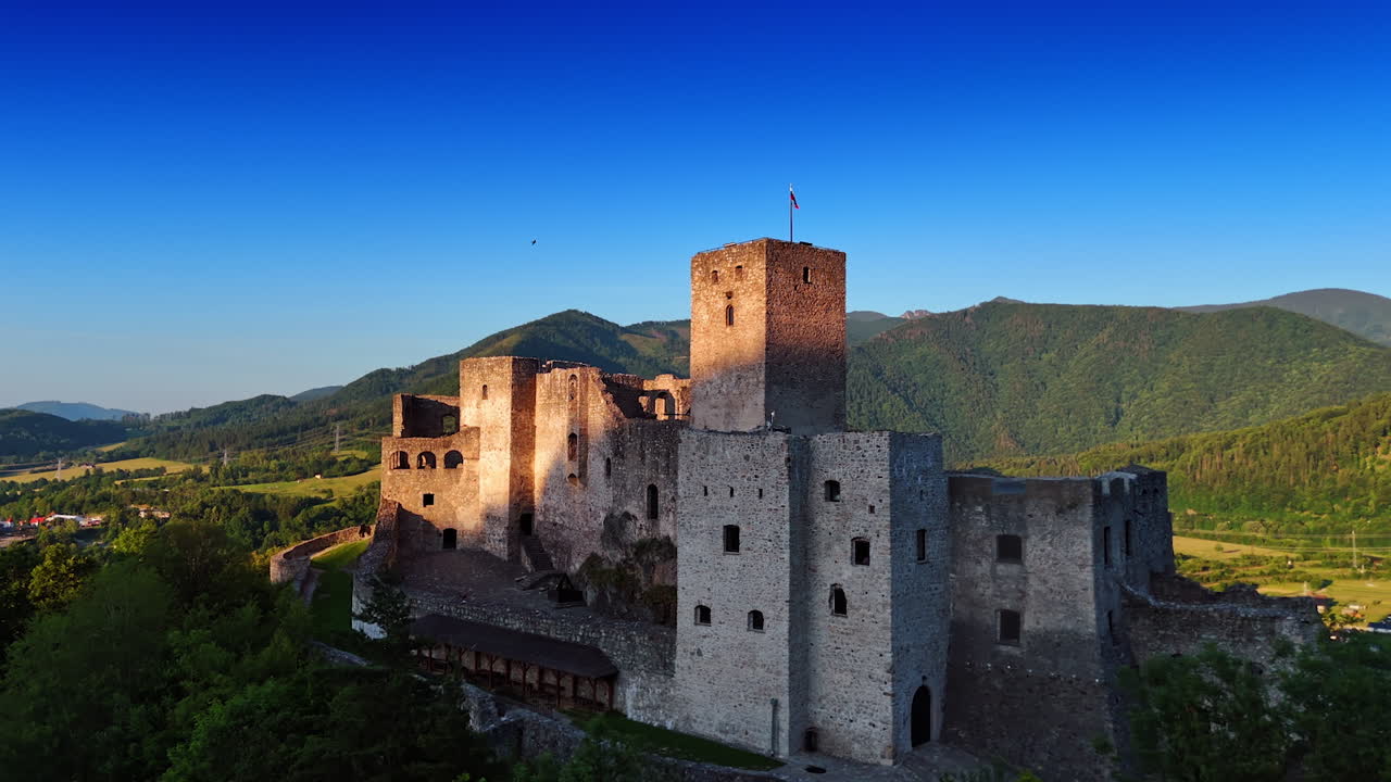 Strecno Castle with a flag on top. Reconstruction of a medieval castle in Slovakia. Green mountains, sunny meadows and river at backdrop. Aerial view.