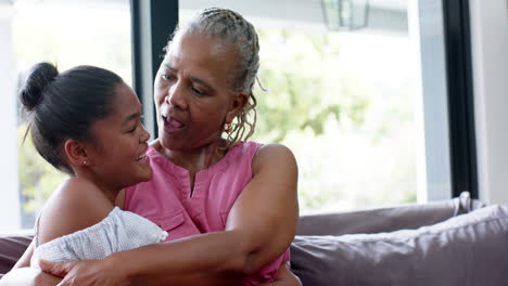feliz nieta afroamericana y abuela abrazándose en el sofá, espacio de copia, cámara lenta