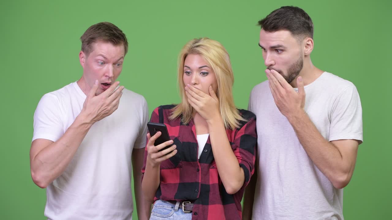 Three young friends using phone together and looking shocked