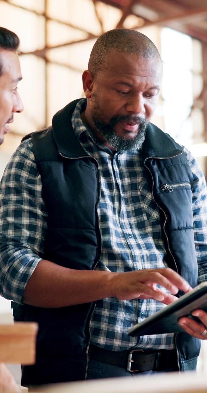 Two Men Discussing Project Details on a Tablet in a Workshop