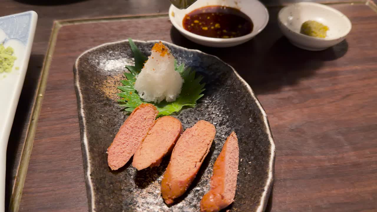 Close-up of sashimi and mentaiko on plates, warm lighting, slow camera pan, restaurant setting