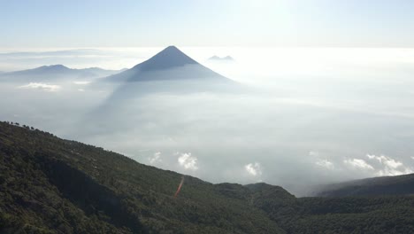 volcanic mountain in the distance, captured with a scenic perspective of rolling hills protruding high above misty haze cloud cover, guatemala