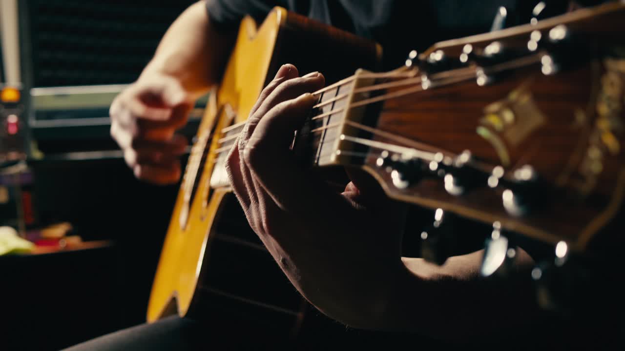 Young musican man checking strings of acoustic guitar close-up. Male guitarist tuning sound of musical instrument.