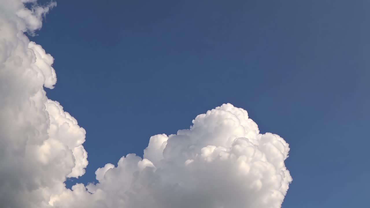A serene video captures fluffy white clouds against a clear blue sky, shot from a low angle