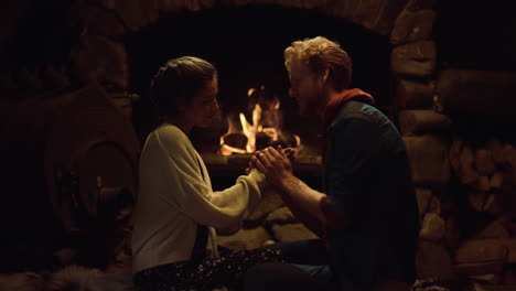 young people hold hands by fireplace. romantic couple spend honeymoon at evening