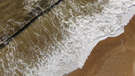 Aerial-looking-down-still-peaceful-golden-colored-beach-from-with-waves-crashing-Bournemouth-UK-English-Channel-surf-Pacific-Ocean-angled-horizon