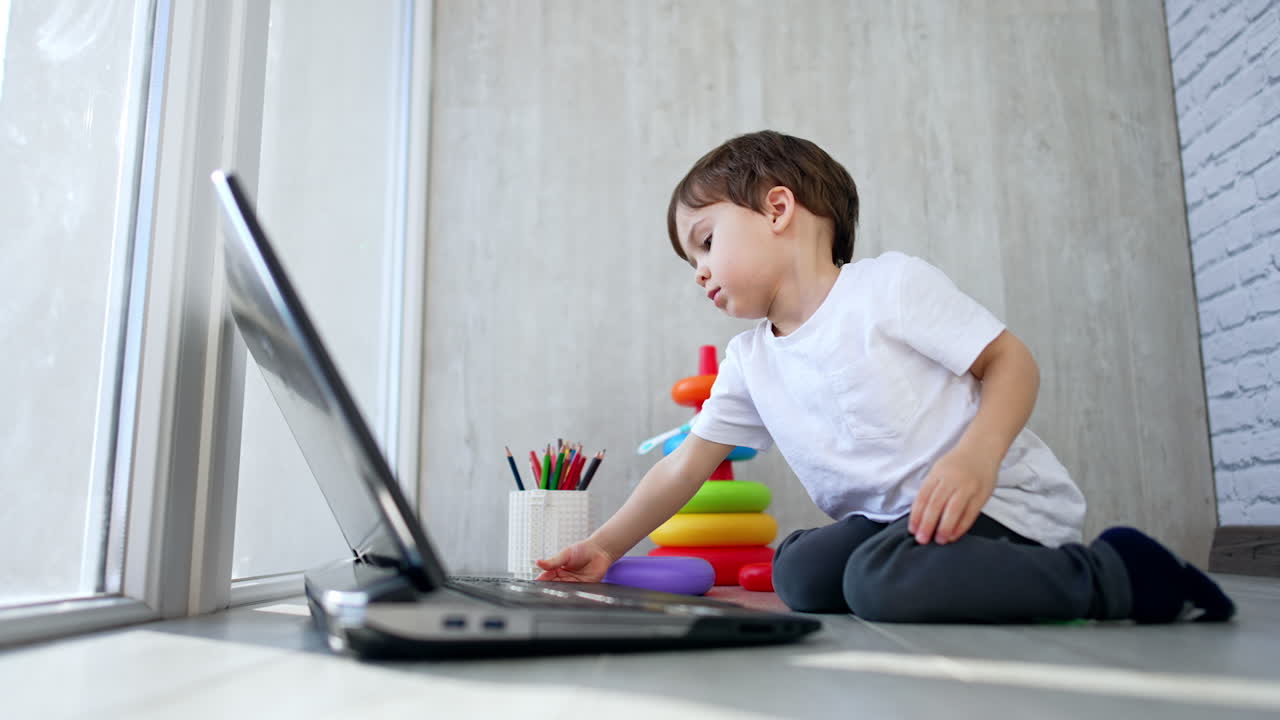 Little kid is focused on the laptop in front of him. Low angle view on the baby interested with gadget.