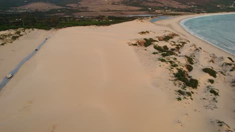 Aerial-view-of-a-wide-sandy-beach-in-Tarifa,-Spain-with-cars-driving-along-the-nearby-road