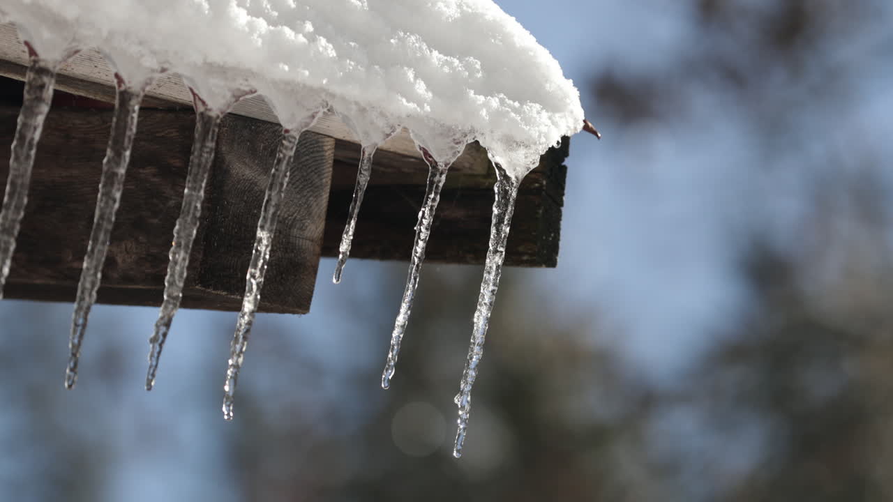 Close-up of melting ice stalactites in Gstaad, Switzerland, with sunlight shining through as water drips gently from the snow, creating a sparkling and serene winter scene