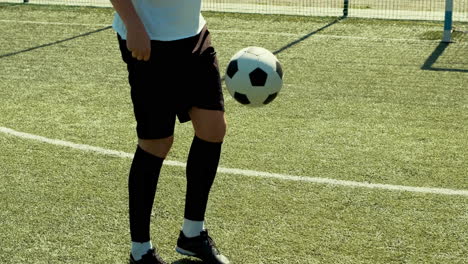 a young soccer man training freestyle tricks with the ball on a street football pitch on a sunny day