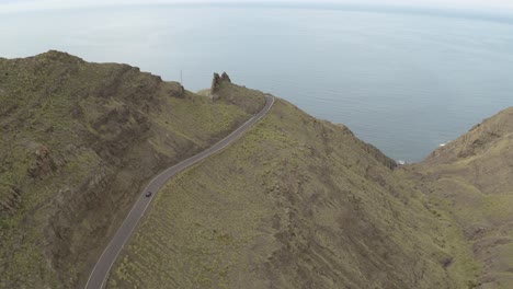 panorama drone shot of a car driving through a road in the mountains and ocean in the background