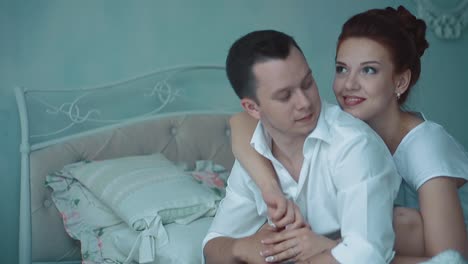 Young-beautiful-couple-sitting-in-the-morning-on-the-bed-looking-out-the-window